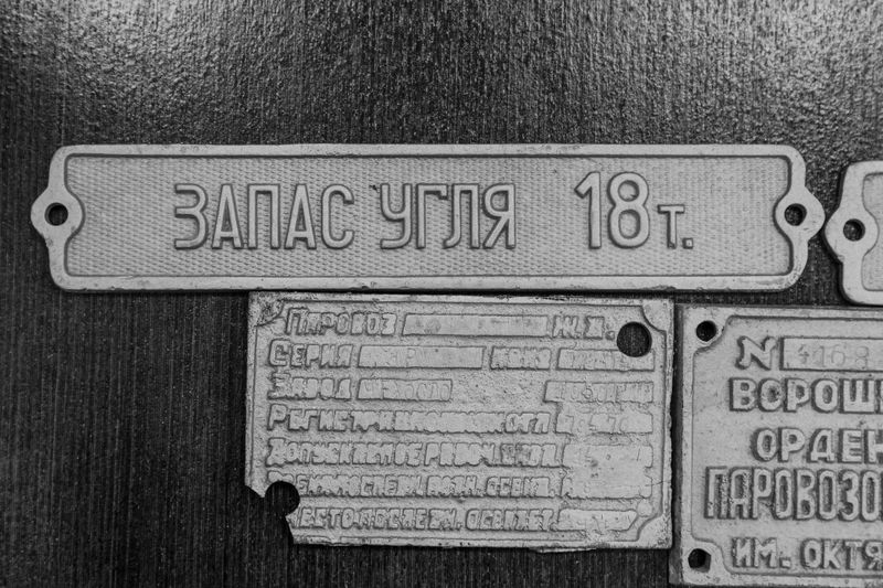 Image en noir et blanc de panneaux métalliques avec du texte en russe, dont un indiquant « Réserve de charbon 18 tonnes ».