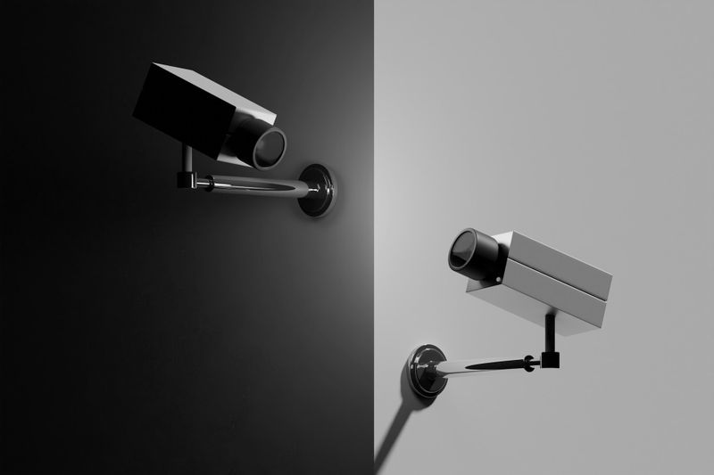 Dos cámaras de vigilancia se enfrentan entre sí sobre un fondo dividido en blanco y negro, creando un efecto visual simétrico y contrastante.