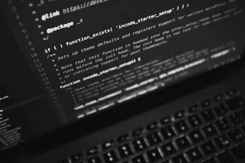Close-up of a laptop screen displaying lines of code in a dark environment, with a keyboard partially visible at the bottom.