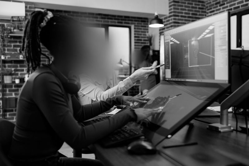 Deux personnes travaillant sur de l'art numérique devant un ordinateur dans un bureau moderne, l'une d'elles pointant vers l'écran. Image en noir et blanc.