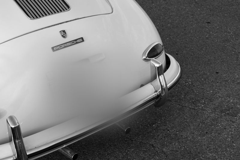Czarno-białe zdjęcie tylnej części klasycznego Porsche pokazujące emblemat, chromowany zderzak, tylną lampę i wydech.