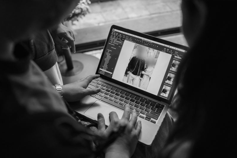 Two people view a photo editing software on a laptop; one points at the screen. The image being edited shows a blurred person.