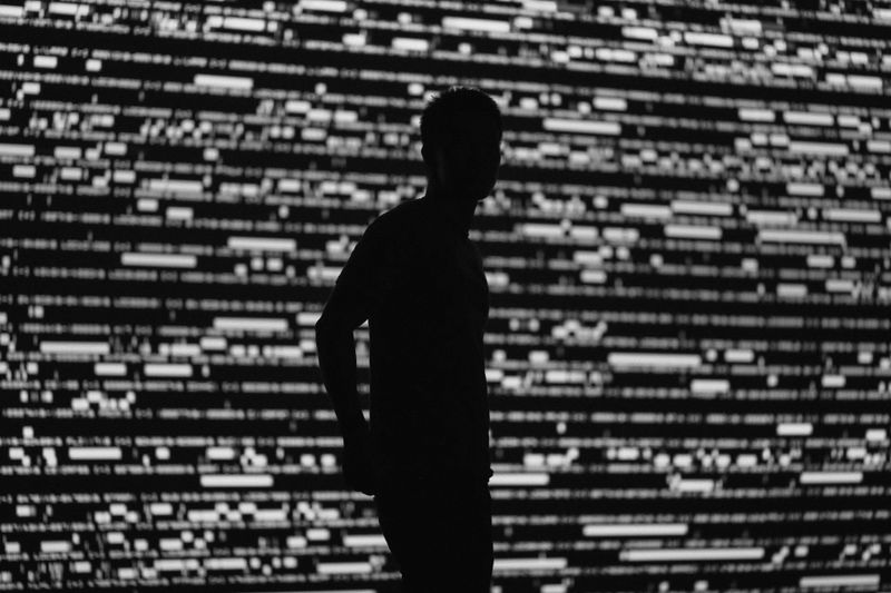 Silhouette d'une personne debout sur un fond de motifs numériques abstraits en noir et blanc.