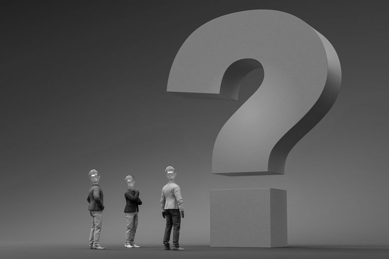 Tres personas con cascos están de pie mirando hacia arriba un gran signo de interrogación 3D sobre un fondo gris liso.