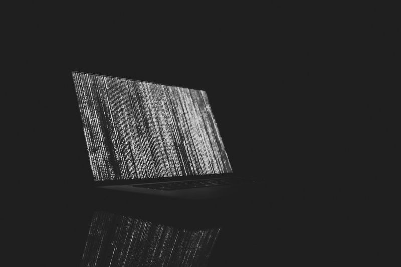 Laptop in a dark room with a glitchy, static-filled screen, casting a faint reflection on a glossy surface.