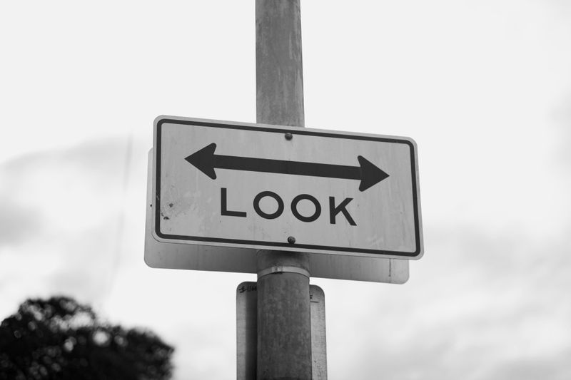 Panneau noir et blanc sur un poteau avec des flèches pointant vers la gauche et la droite, affichant le mot « REGARDER ».