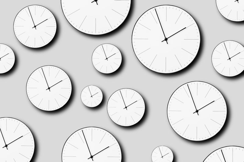 Varios relojes analógicos blancos con manecillas negras mostrando diferentes horas sobre un fondo gris claro.