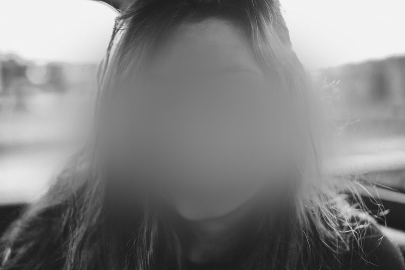 A black and white photo of a person with their face obscured by a blur effect, sitting inside a vehicle.