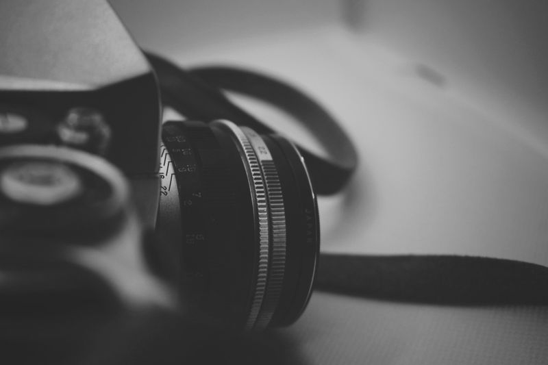 Gros plan d'un appareil photo vintage en noir et blanc, mettant l'accent sur l'objectif et une partie du corps avec un arrière-plan flou.