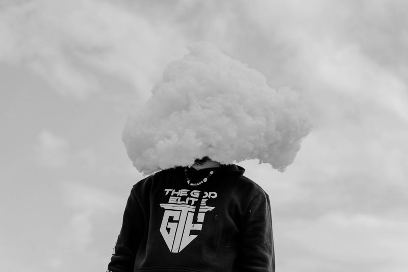 Personne portant un sweat à capuche avec un nuage obscurcissant sa tête, sur fond de ciel nuageux en noir et blanc.