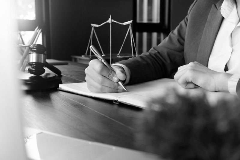 Une personne tamponne un document sur un bureau, tenant un tampon d'une main et reposant l'autre sur le papier. Photo en noir et blanc.