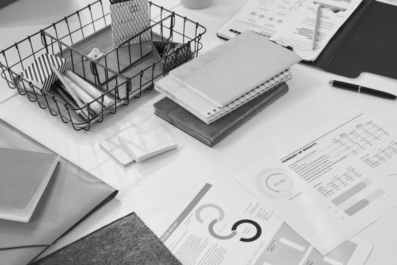 A black-and-white desk with notebooks, documents, a wire basket, pens, and charts, suggesting an organized yet busy workspace.