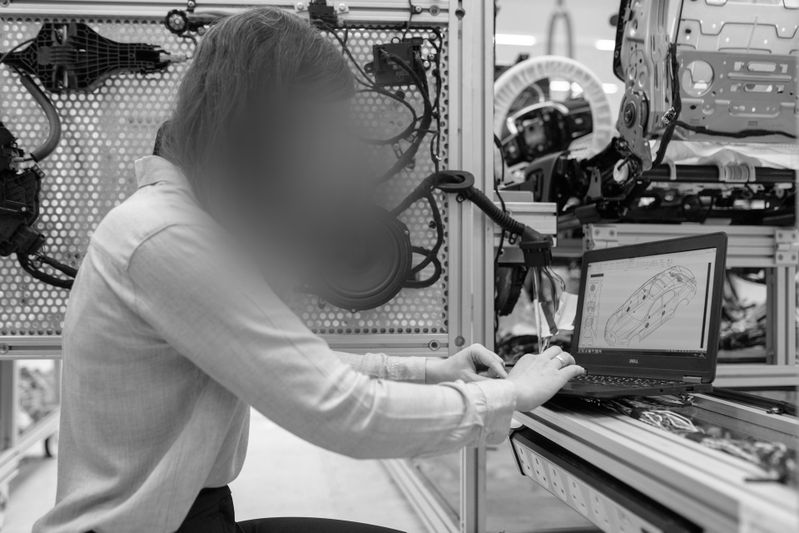 Person arbeitet an einem Laptop in einer industriellen Umgebung, schaut sich Diagramme an, umgeben von Maschinen und Geräten.