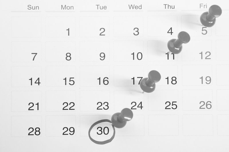 Un calendrier avec des punaises plantées dans les vendredis et un cercle marquant le 30e jour du mois. Les noms des jours de la semaine sont inscrits en haut.
