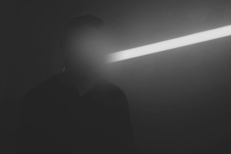 Silhouetted person in foggy, dim lighting with a bright horizontal light beam obscuring their face.