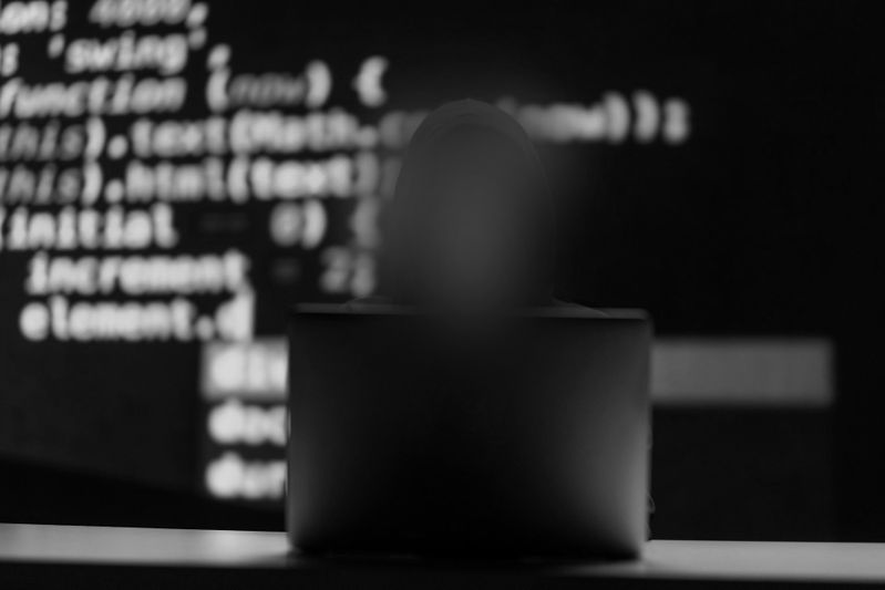 Silhouette d'une personne devant un ordinateur portable, avec un code informatique flou projeté sur un écran en arrière-plan.