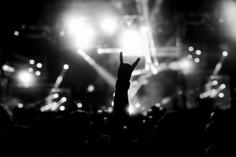 Silhouette of a raised hand making a rock sign against bright stage lights at a concert.