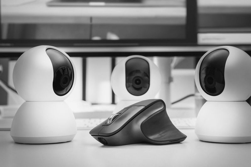 Tres cámaras de seguridad redondas frente a un ratón de computadora ergonómico moderno sobre un escritorio en un entorno monocromático.