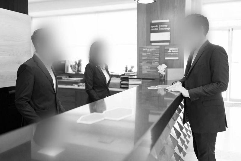 Des personnes en costume, aux visages floutés, discutent à une réception moderne dans un décor monochrome.