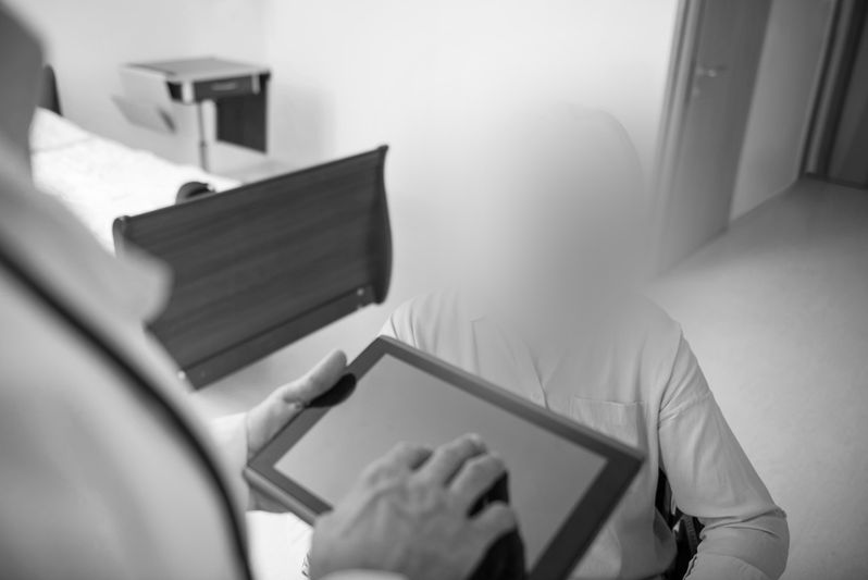 Un doctor mostrando una tableta a un paciente en una habitación de hospital, con sus caras borrosas.