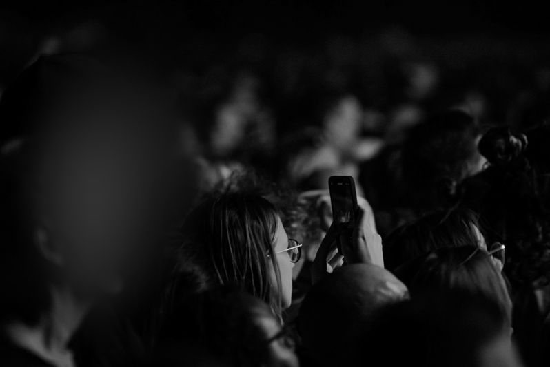 Black and white photo of a crowd at a concert, with a person holding up a phone to capture the moment.