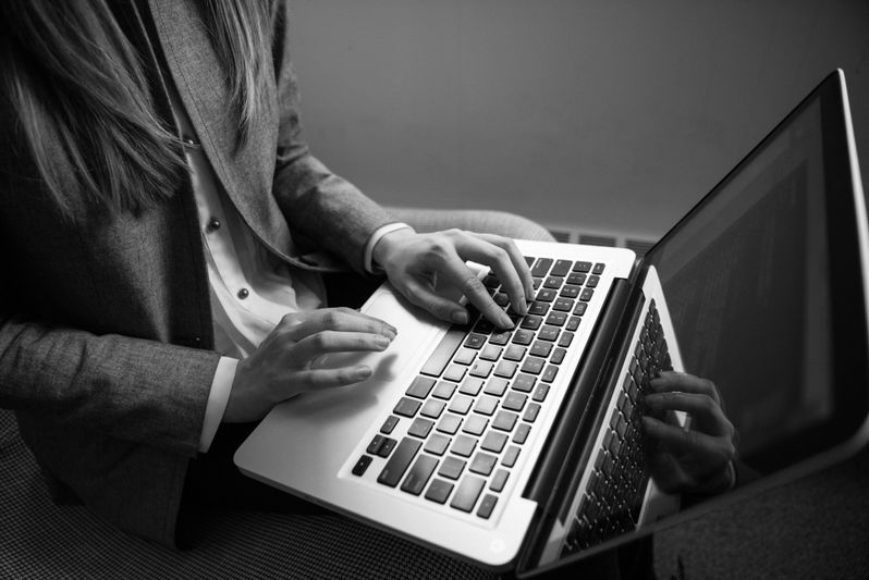 Personne tapant sur un ordinateur portable, vêtue d'une veste de costume. L'image est en noir et blanc, mettant en valeur les mains et le clavier.