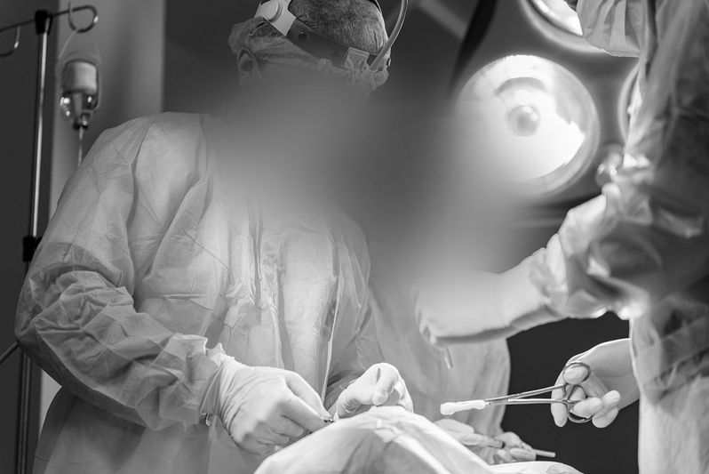 Surgeons in scrubs perform a procedure under bright surgical lights in an operating room, with medical instruments in use.