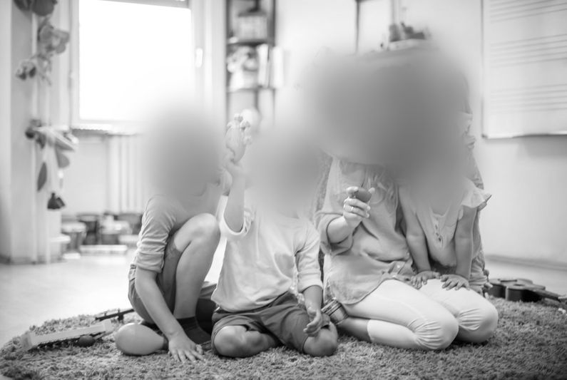 Un groupe d’enfants est assis au sol autour d’un adulte lisant un livre dans une salle de classe. L’image est en noir et blanc.