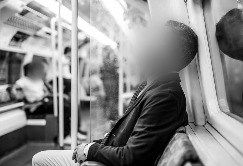 Une personne floue s'appuie contre une fenêtre de métro, assise dans une voiture vide. L'intérieur est doucement éclairé, avec des reflets sur le verre.