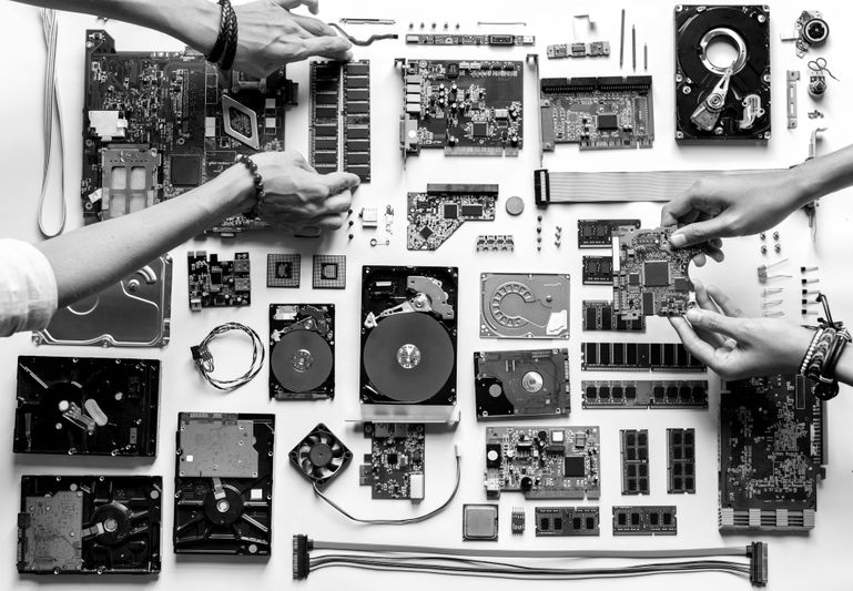 Verschiedene Computerhardware-Komponenten und Leiterplatten ordentlich auf einer weißen Fläche angeordnet. Zwei Hände sind beim Zusammenbauen von Teilen zu sehen.