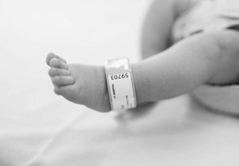 A black-and-white photo of a newborn's foot with a hospital ID band, set against a soft blanket.