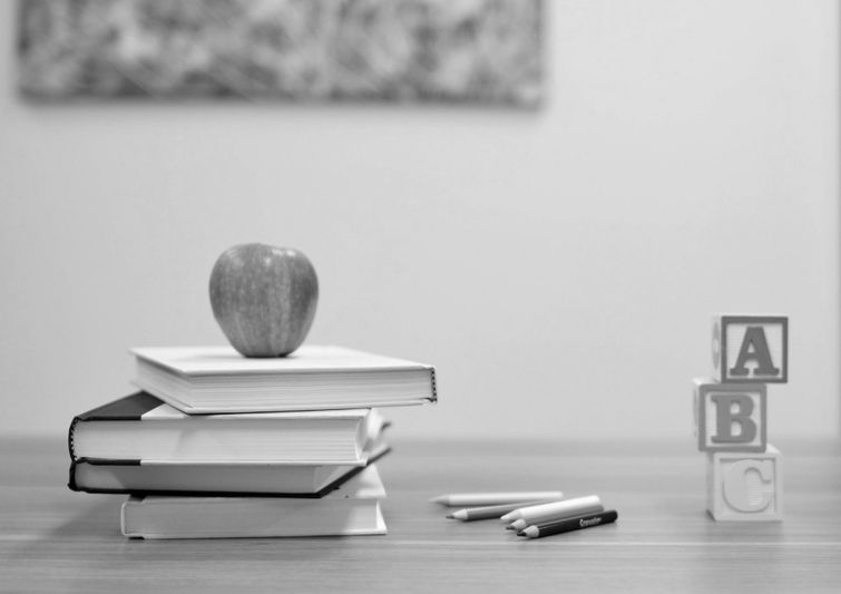 Image en noir et blanc d'une pomme sur des livres empilés, des crayons et des blocs ABC sur une table en bois.