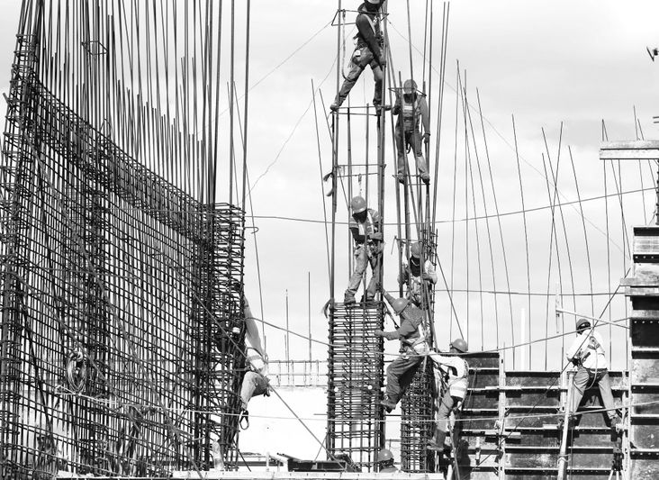 Des ouvriers du bâtiment grimpent et assemblent des armatures en acier sur un chantier. Architecture minimaliste sur fond de ciel dégagé.