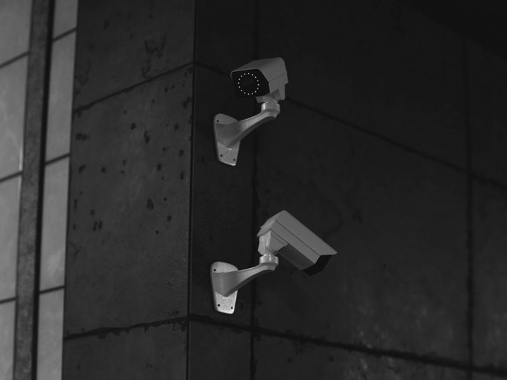 Deux caméras de surveillance montées sur un mur carrelé sombre, l'une tournée vers l'avant et l'autre inclinée vers le bas.