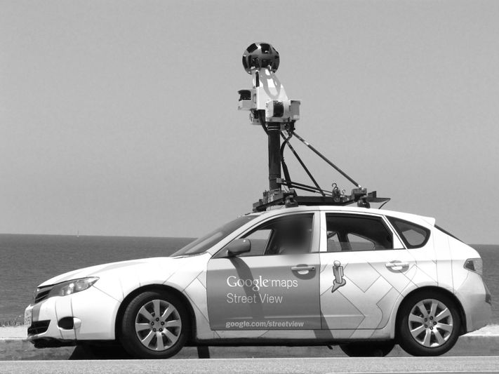 Voiture Google Maps Street View avec caméra embarquée, garée au bord de l'océan, capturant des images panoramiques. Photo en noir et blanc.