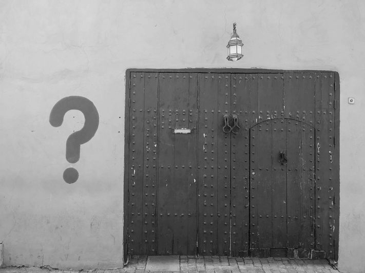 Fotografía en blanco y negro de una puerta de madera, con un signo de interrogación a la izquierda.