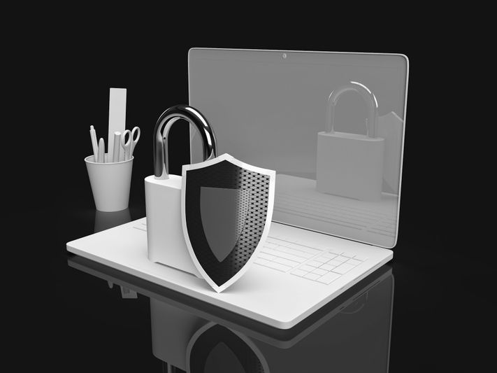 A laptop with a large padlock and shield symbol on the keyboard, symbolizing cybersecurity. A cup with stationery is beside it.