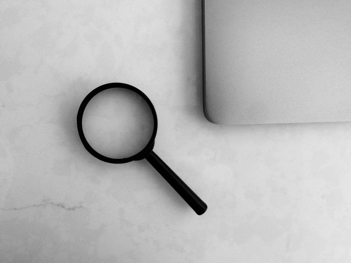 Une loupe noire sur une surface en marbre blanc à côté du coin d'un ordinateur portable argenté.