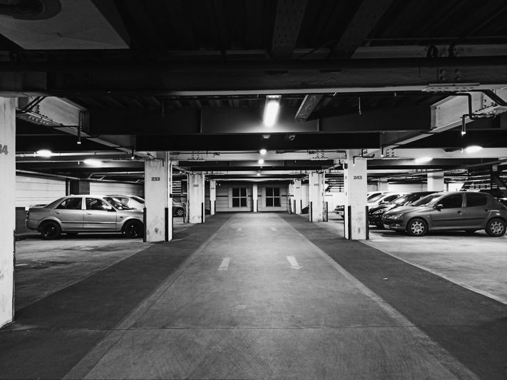 Image en noir et blanc de la sortie vide d’un parking couvert, avec des barrières abaissées et des panneaux de sortie lumineux au-dessus.
