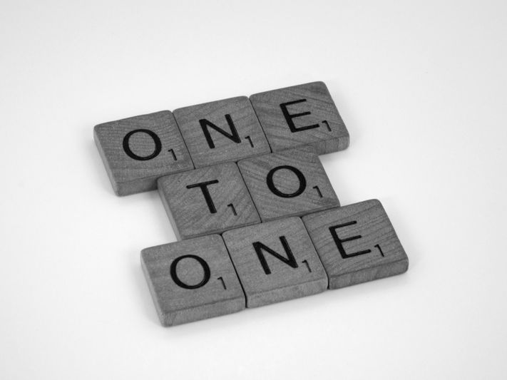 Tuiles de Scrabble disposées pour épeler « ONE TO ONE » sur un fond blanc.