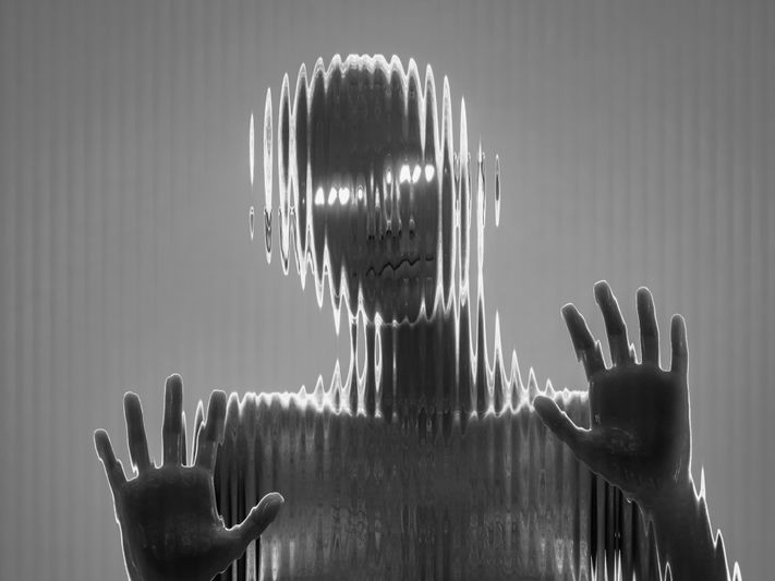 Silhouette déformée d'une personne avec les mains pressées contre une surface de verre ondulée, créant un effet visuel surréaliste et ondulé.
