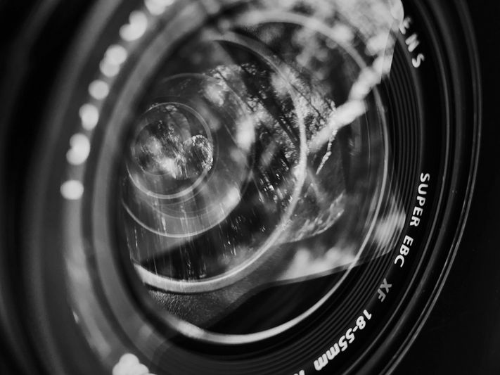 Gros plan sur un objectif d'appareil photo avec des reflets et des marquages visibles, notamment « SUPER EBC XF 18-55 mm ». L'image est en noir et blanc.