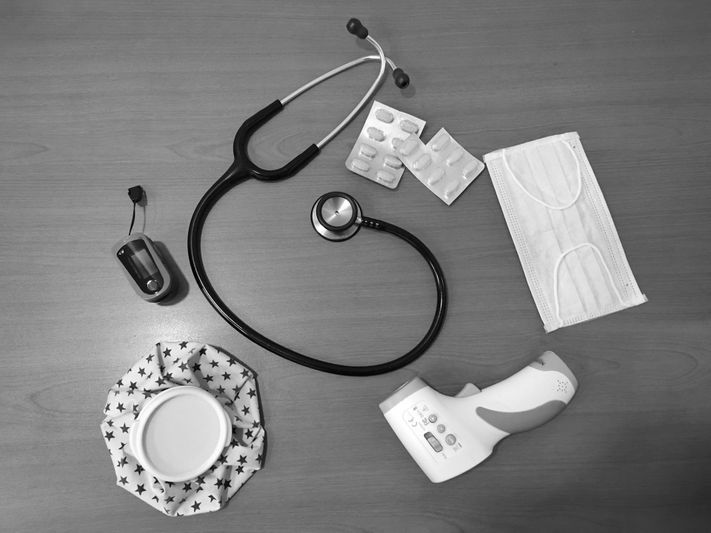 Articles médicaux sur une table : stéthoscope, thermomètre, pilules, masques faciaux, tasse sur une soucoupe à motif d'étoile et un petit récipient.