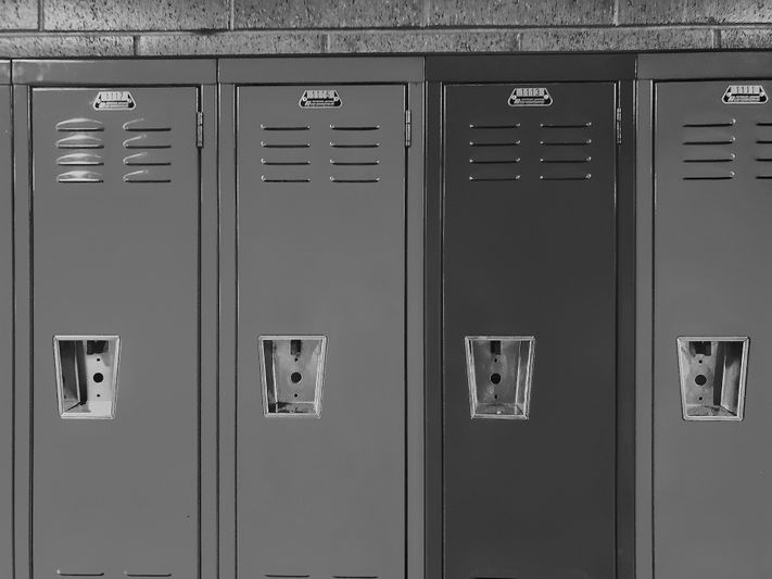 Photo en noir et blanc de quatre casiers d'école avec des fentes d'aération et des serrures à combinaison, placés contre un mur de briques.