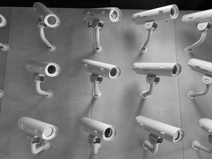 Multiple white security cameras mounted in rows on a wall, angled downward in a repeating pattern.