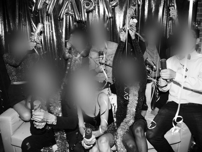 Group of people celebrating with confetti and party poppers, seated on a couch with festive decorations in the background.
