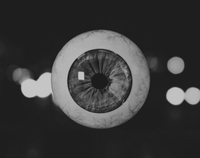 A grayscale image of a human eye with detailed iris and pupil, set against a blurred background with circular light bokeh.