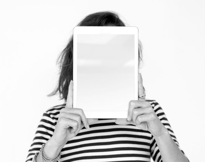 Personne en chemise rayée tenant une tablette devant son visage, masquant ses traits sur un fond blanc uni.
