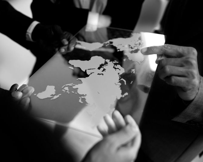 Des personnes tenant une carte du monde réfléchissante, pointant vers différentes régions, dans un décor monochrome.
