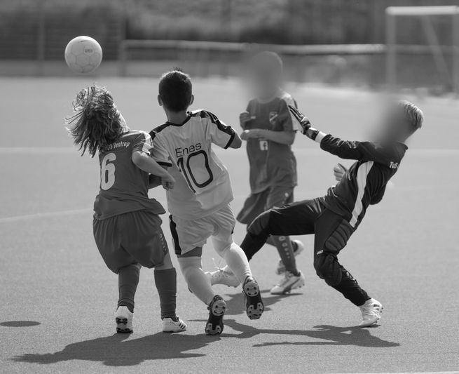 Children playing soccer on a field, two players in red and two in white and black jerseys, actively competing for the ball.